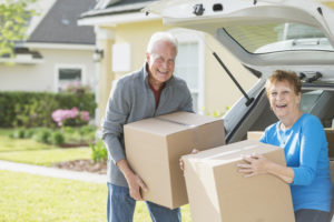 A happy senior couple moving boxes into or out of the back of their car. They are moving house, perhaps downsizing. They are looking at the camera, smiling.